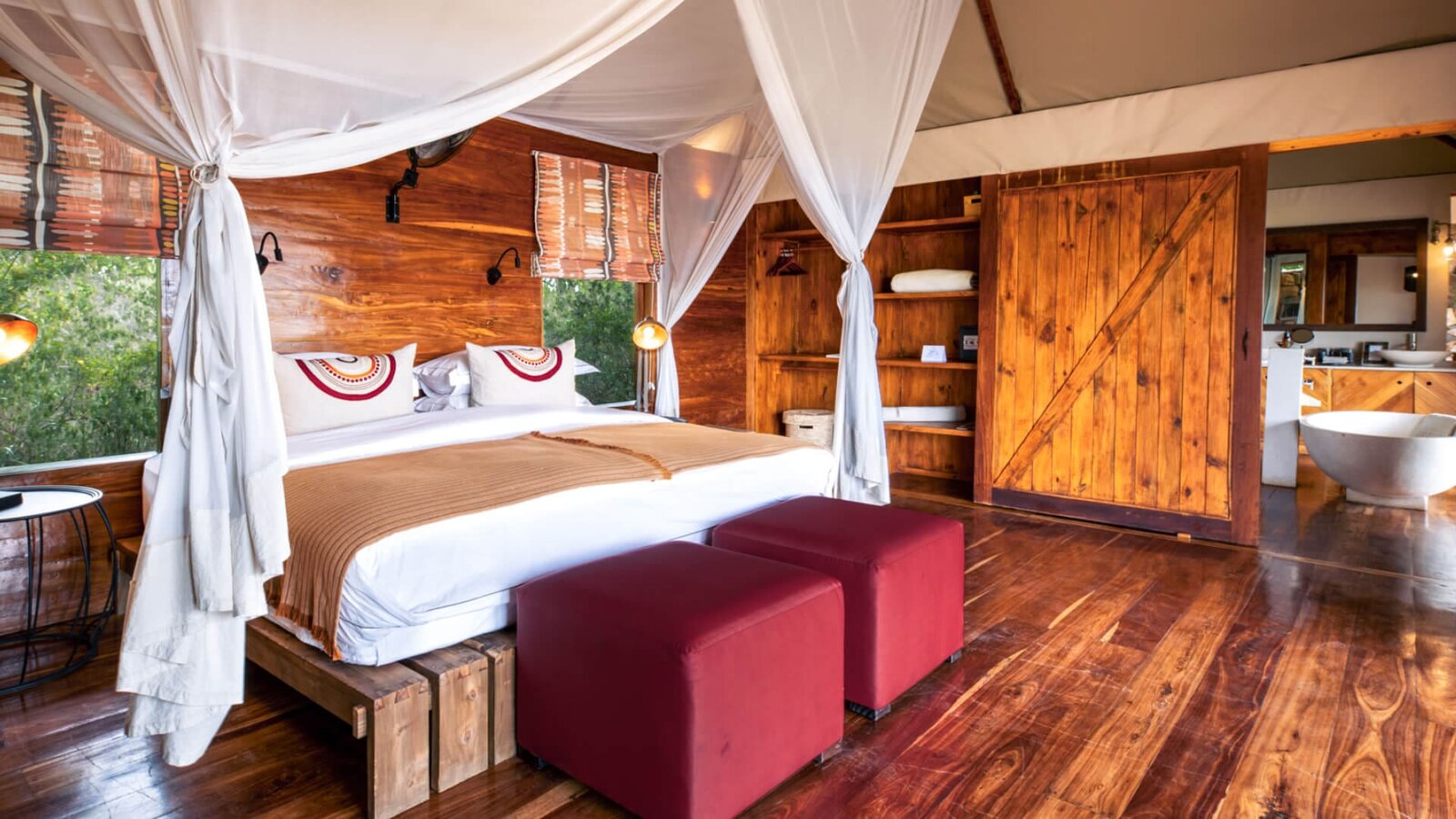 Elevated tented suite interior at Sayari Camp with a canopy bed and warm timber finishes