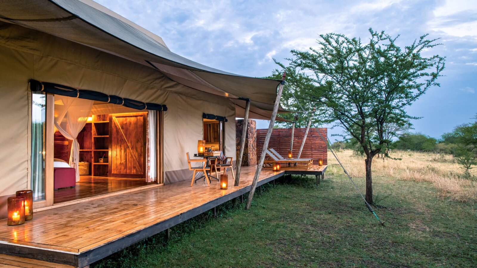 Sayari Camp guest tent exterior raised on a deck beneath acacia trees on the Serengeti plains