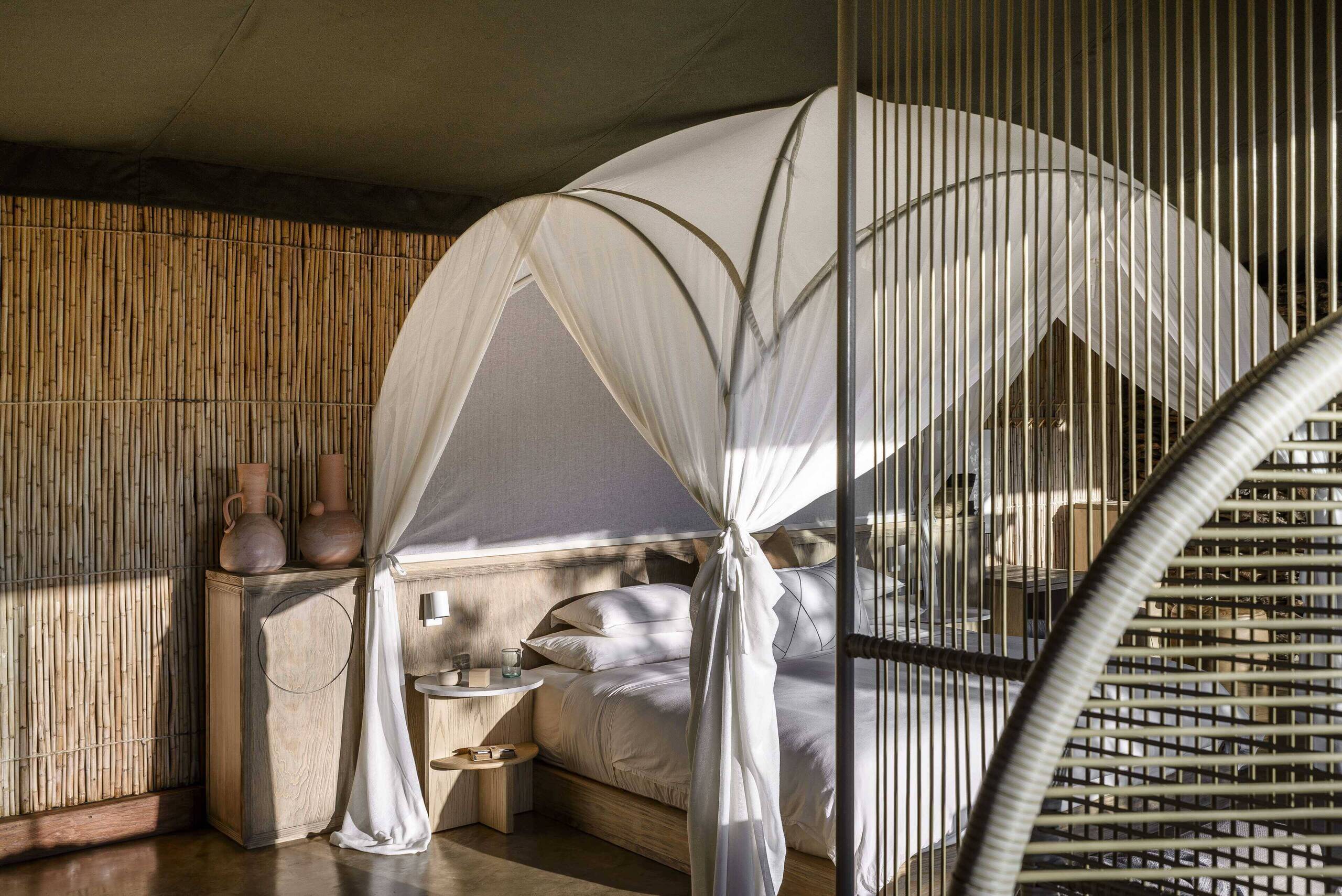 Inside a Faru Faru suite — king bed, botanist's-camp styling, floor-to-ceiling glass onto the Grumeti River.