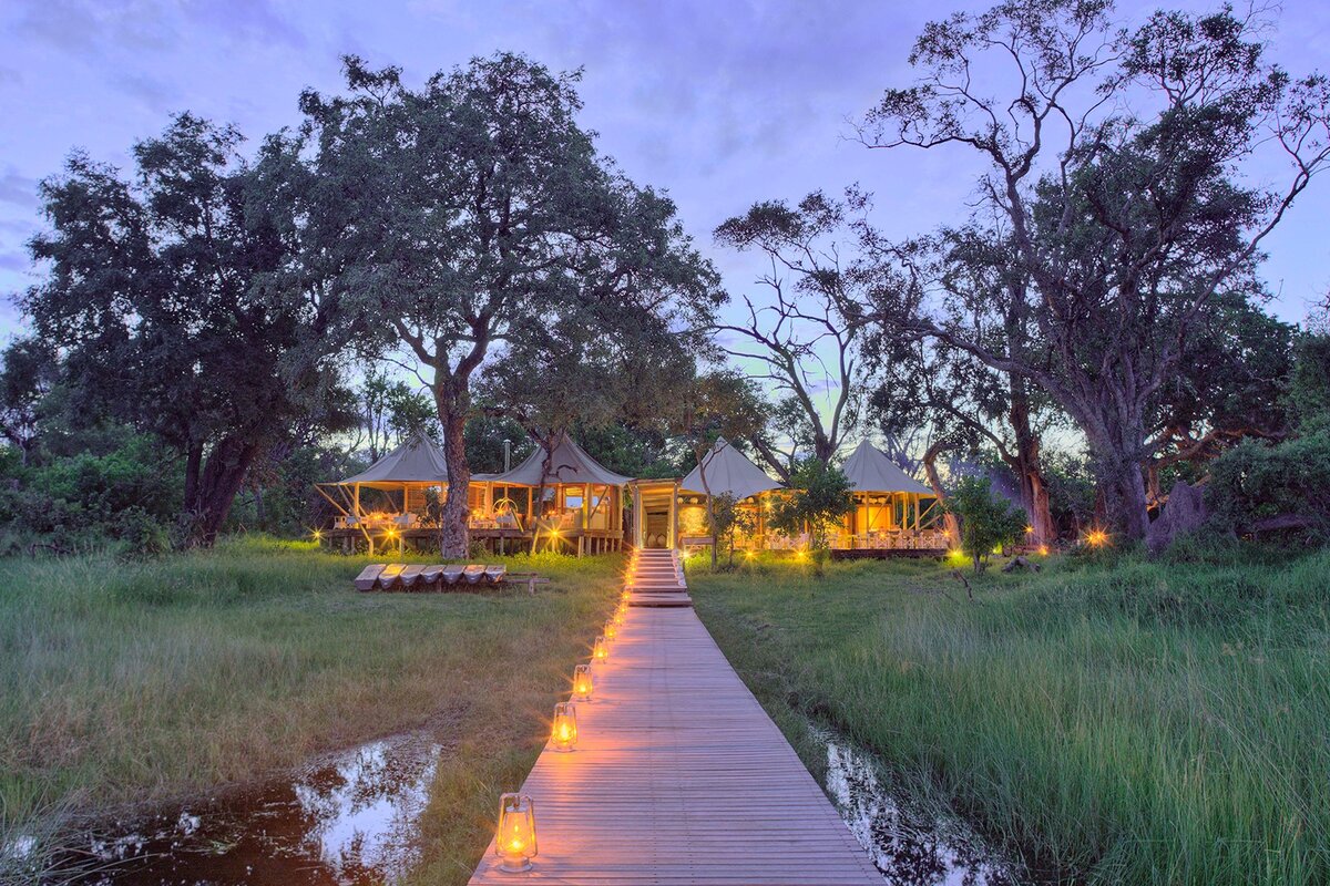 Xaranna Okavango Delta Camp stilted suites along a wooden walkway at dusk