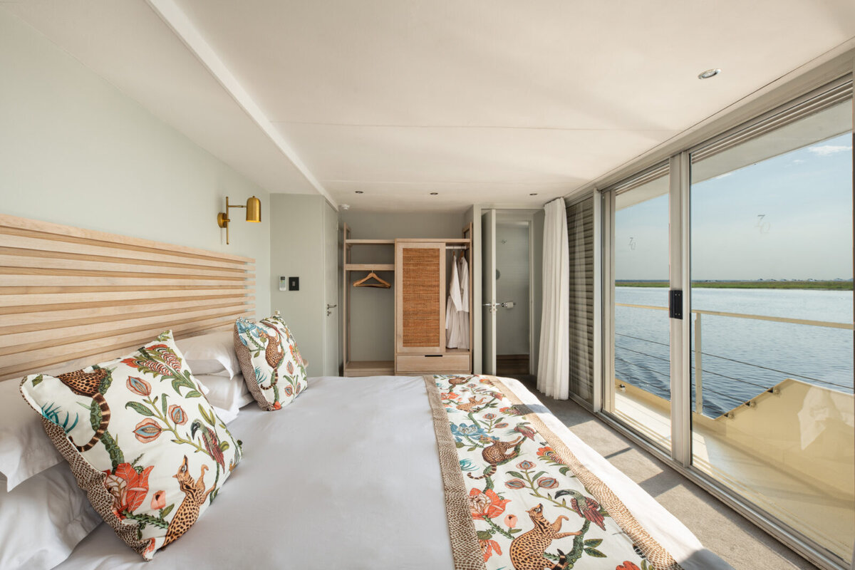 An elegant all-suite cabin aboard the Zambezi Queen luxury houseboat with a king bed and floor-to-ceiling windows over the Chobe River