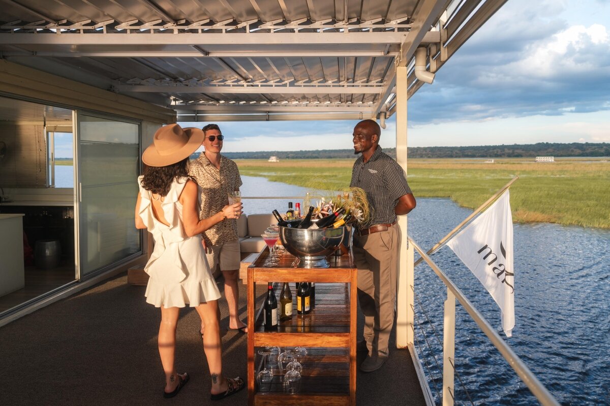 Sundowner drinks served on the private deck of a luxury Chobe River houseboat at golden hour