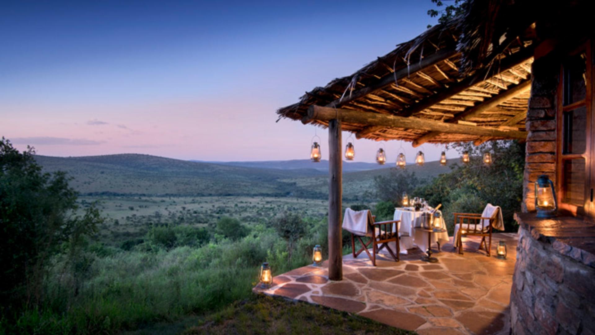 andBeyond Klein's Camp lantern-lit cottage terrace overlooking the Serengeti at dusk